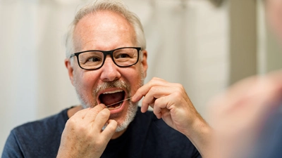 Un homme utilise du fil dentaire pour éviter des problèmes de déchaussement des dents.