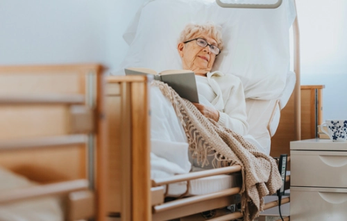 femme âgée allongée sur un lit d'hôpital, en train de lire un livre