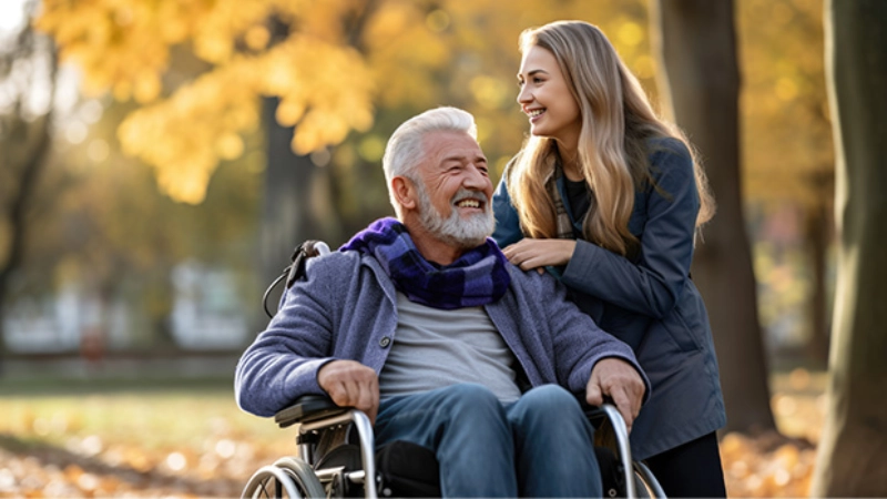 Une jeune femme souriante aidant un vieil homme souriant en chaise roulante